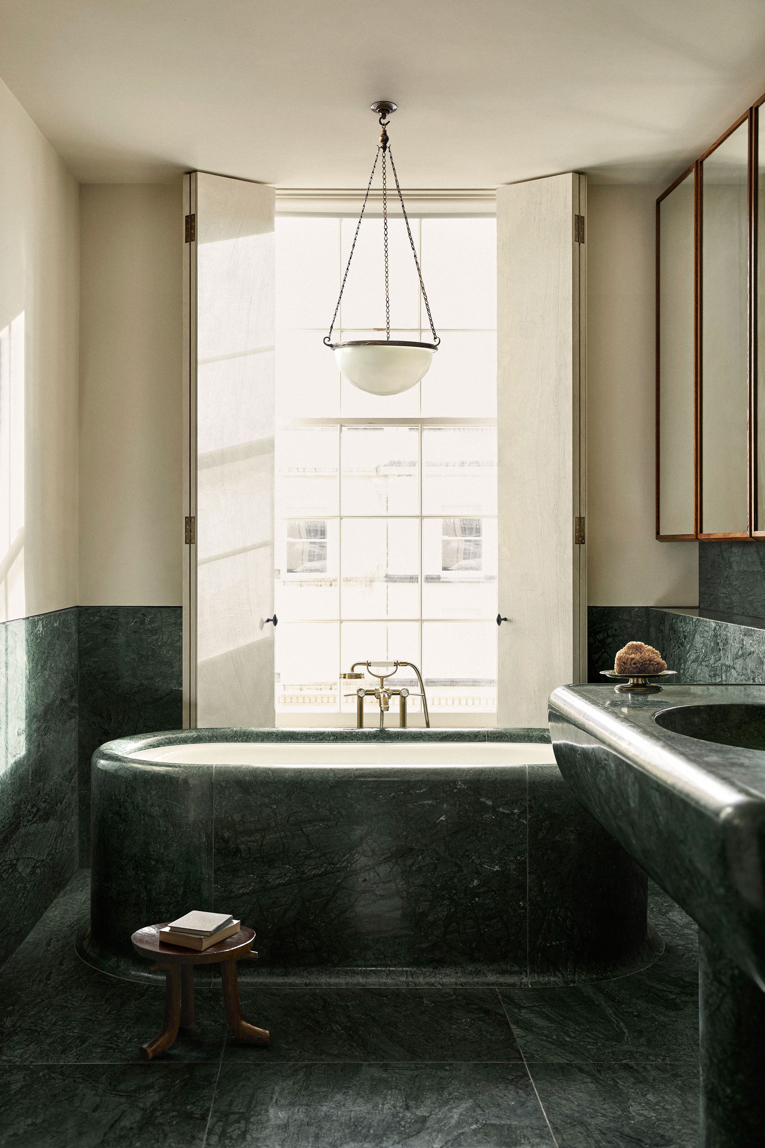 Antique 1930’s ‘Moonstone’ milk glass Plafonnier light. Marble bathtub &amp; vanity counter: Custom-designed by Child Studio in Green Verde Guatemala marble. Early 20th century Ethiopian hand-carved three-legged wooden stool.
Photography by Helen Cathcart.