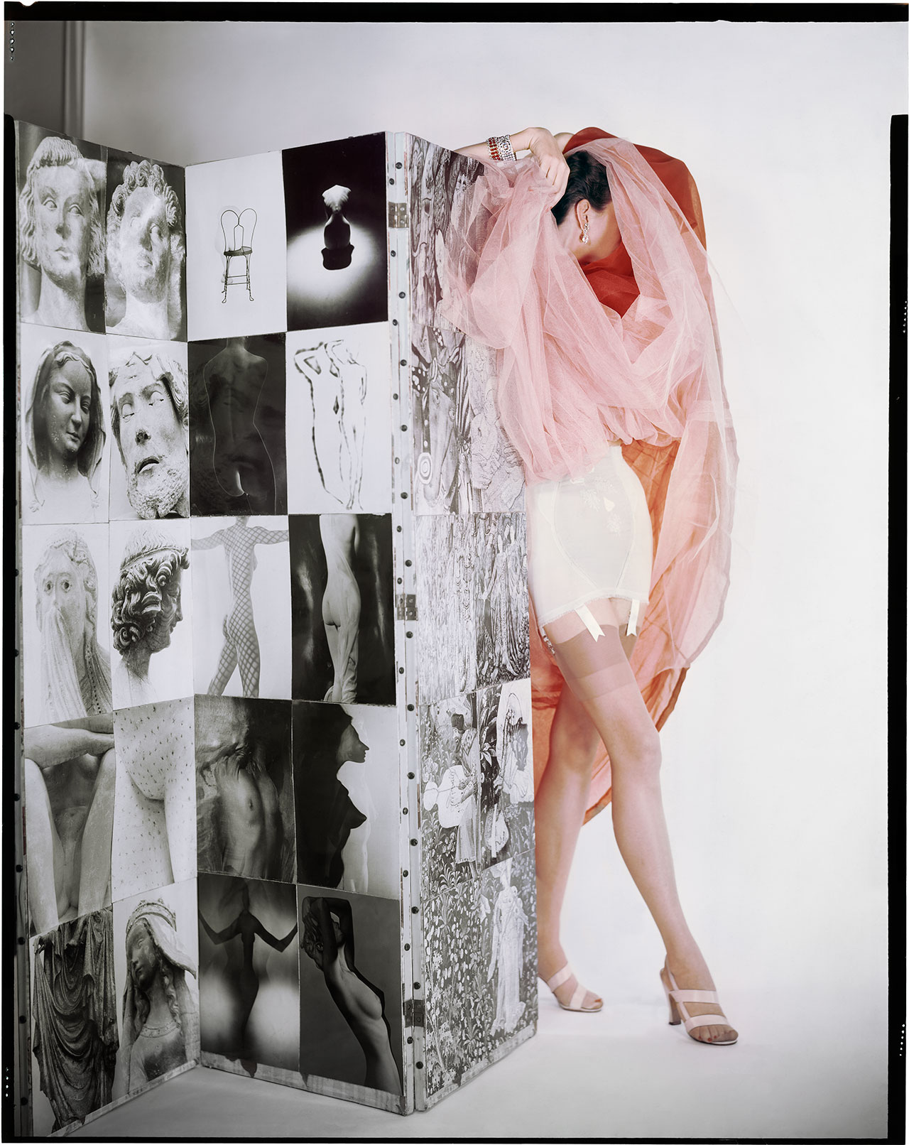 Lily of France Corset, Dior Organdi, Modeltex Low, Valley Sandals. Model: Ruth Knowles. In front of a screen of photographs by Erwin Blumenfeld. Variant of the photograph published in Vogue US February 15, 1953 © The Estate of Erwin Blumenfeld.